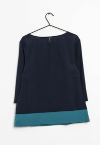 Túnica marina con dobladillo en tono teal, que presenta mangas largas y un escote ligeramente ancho. Cierre con cremallera en la parte posterior y detalle de pliegue en la parte superior.