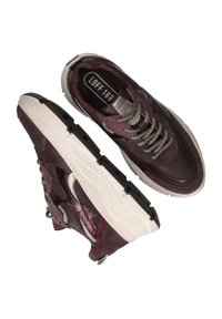 Une paire de baskets violet foncé avec des lacets à motifs blancs et noirs, des panneaux latéraux texturés et des semelles blanches épaisses, montrée avec des vues de dessus et de côté.