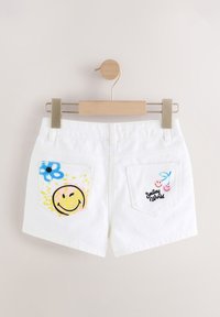 Shorts di denim bianco con grafiche colorate. Una tasca presenta una faccina sorridente e un fiore; l'altra mostra la scritta "Smiley World" e delle ciliegie.
