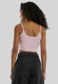 Lys rosa cropped tank topp med tynne stropper, sammen med høytlivs svarte denimbukser med to baklommer. Glatt tekstur.