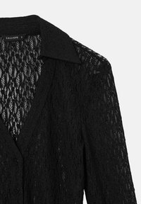 Schwarze Spitzenbluse mit kragenförmigem Ausschnitt, Knopfverschluss und transparenter Textur. Mit einem floralen Muster über den gesamten Stoff. Größe S.