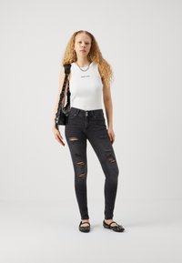 Crne poderane skinny traperice s visokim strukom, uparene s bijelim bezrukavnim topom na kojem piše "PRAVA LJUBAV" i crnim ravnim cipelama sa čavlima.