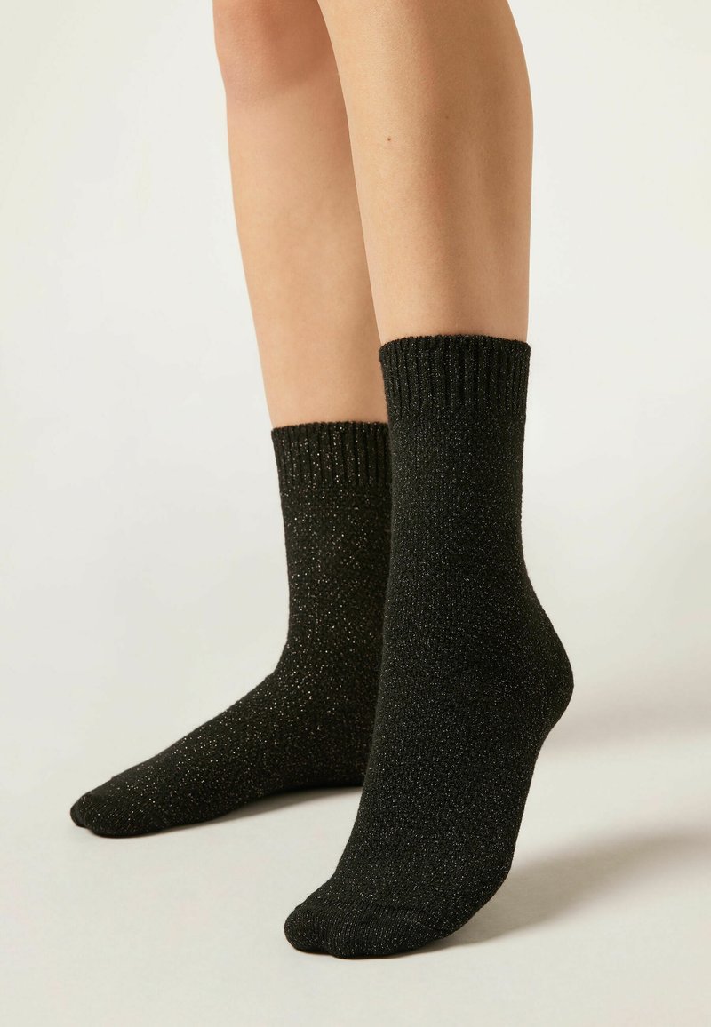 Chaussettes noires avec une finition côtelée, en matériau texturé avec des paillettes subtiles, se situant juste au-dessus de la cheville.