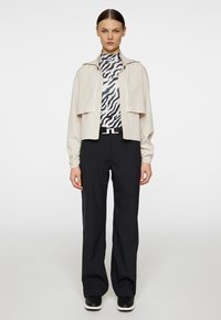 Beige cropped jack met een knopenfront, gelaagd ontwerp; zwart-witte gestreepte coltrui; zwarte wijde broek; zwarte schoenen met witte zolen.