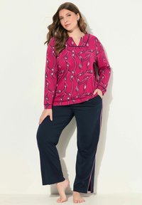 Fuchsia pyjamajack met lange mouwen en abstracte witte en blauwe patronen, gecombineerd met marineblauwe broek met roze zijstrepen.