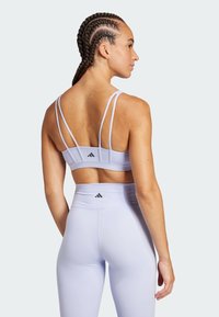 Sujetador deportivo de color púrpura claro con tirantes finos y detalle de logo, combinado con leggings de alta cintura en el mismo color. Tela lisa y elástica.