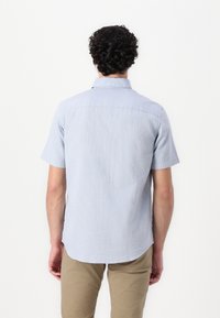 Camicia azzurra chiara a maniche corte con un motivo testurizzato, colletto con bottoni e orlo arrotondato, indossata con pantaloni khaki.