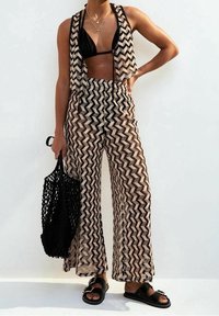 Dvoudílný outfit složený z odhaleného přehozu se vzorem chevron a širokých kalhot s potiskem. Černý bikiny top a černé sandály dokončují vzhled.