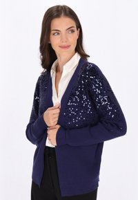 Marineblauer Cardigan mit Paillettenärmeln, langen Ärmeln, offener Vorderseite, gerippten Bündchen und Saum; der weiche Strickstoff steht im Kontrast zu den glänzenden Pailletten.