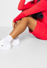 Czerwona koszulka sportowa z długim rękawem, dopasowane czerwone szorty, białe sneakersy Nike i białe skarpetki sięgające za kostkę. Gładka tekstura o dopasowanym kroju.