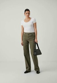 Top blanco de manga corta con canalé, pantalones de pierna ancha color verde oliva, bolso pequeño negro, zapatos negros, collar de cadena dorada, diseño sencillo.