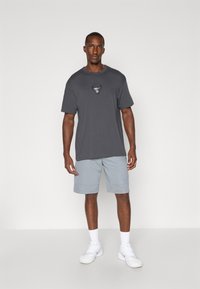 Grå bomulls T-skjorte med en tyre graphic på brystet, parret med lysegrå shorts og hvite sportsko. Minimalistisk design og vanlig passform.