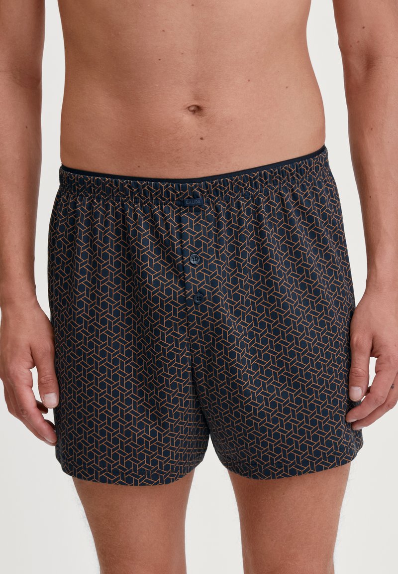 Marineblauwe boxers met een geometrisch patroon in oranje, voorzien van een elastische tailleband en drie knopen aan de voorkant van de gulp.