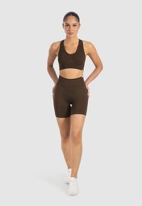 Ruskea urheiluliivit ja korkeavyötäröiset shortsit, valmistettu sileästä kankaasta. Setissä on istuva malli ja tyylikäs siluetti. Valkoiset lenkkarit.