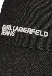 Melnas denima cepure ar izšūtu "KARL LAGERFELD JEANS" logotipu baltā krāsā. Strukturēts dizains ar teksturētu audumu un izliekto malu.