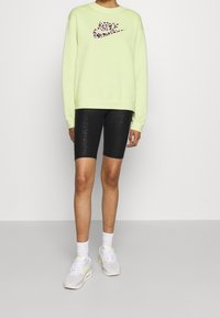 Lichtgroene sweatshirt met een roze luipaardprint Nike-logo, gecombineerd met zwarte gestructureerde fietsbroekjes en witte sneakers met pastelaccenten.