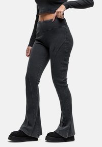 Hoge taille, zwarte flared broeken met een gladde textuur, voorzien van gebogen naaddetails en contrasterende stiksels. Gestyleerd met zwarte plateau schoenen.