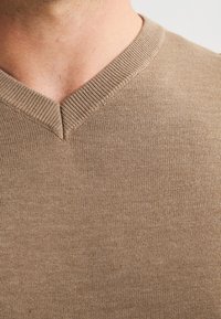 Pulover maro cu decolteu în V, cu un guler texturat, textură fină și material tricotat, arătând un prim-plan al țesăturii și detalii ale gulerului.