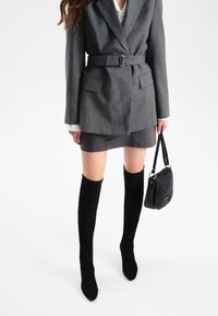 Szary marynarka w kratę z paskiem, w połączeniu z czarną mini spódnicą i czarnymi, materiałowymi kozakami za kolano. Dodatki w postaci czarnej torebki.
