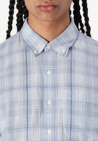 Light blue checkered button-up shirt made of soft fabric, featuring a classic collar, two front buttons, and a single chest pocket.