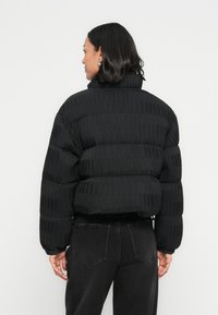 Μαύρο μπουφάν τύπου puffer με ριμπ υφή, cropped σχεδιασμό, ψηλό γιακά και ελαστικά μανσέτες. Συνδυάζεται με μαύρο τζιν για αρμονική εμφάνιση.