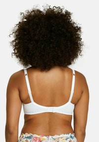 Bra bianco con texture liscia, dotato di spalline regolabili e chiusura con gancio. Il retro presenta bordi ondulati e dettagli minimi.