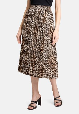 Femme portant une jupe plissée mi-longue à imprimé léopard et des sandales noires à talons hauts avec des bretelles fines.