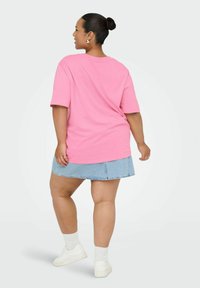 Camiseta oversized rosa de manga corta, combinada con una falda de mezclilla azul clara. Zapatillas blancas y calcetines tobilleros. Textura de algodón suave.