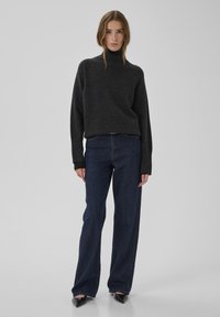 Tumši pelēks džemperis ar augstu apkakli un ribveida aprocēm, kopā ar platajiem tumšā džinsa biksēm. Modelis valkā melnas kurpes ar smailu purngalu.