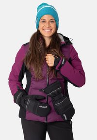 Veste de ski violette avec des accents noirs, doublure grise et gants amovibles. Un bonnet tricoté bleu avec des rayures blanches complète le look.