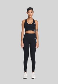 Zwarte sportbh met een v-hals en drie banden, gecombineerd met hoge zwarte leggings. Beide items hebben een wit logo.
