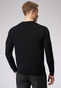 Maglione nero a maniche lunghe in maglia con scollo rotondo e polsini a costine. Texture liscia, design minimalista e silhouette aderente.