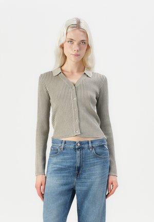 Beige ribbed cardigan with a collared neckline and button closure, paired with blue jeans; features long sleeves and a cropped fit.