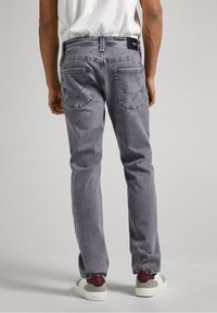 Jeans de denim gris con corte de pierna recta, bolsillos traseros con un patrón de costura único y una etiqueta en la cintura. Diseño simple, sin adornos.