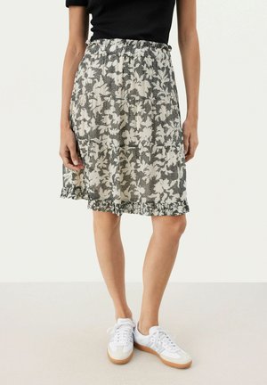 Blommönstrad kjol i svart och vitt, med en samlad elastisk midja och volang i nederkant, kombinerad med vita sneakers.