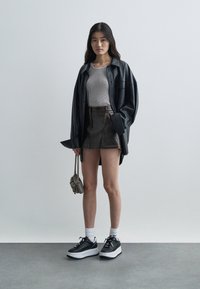 Must mustaari oversize-särk, hall soonitud kampsun, tume teksaseelik, valged platvormtennid ja väike struktureeritud kott ketispidemega.