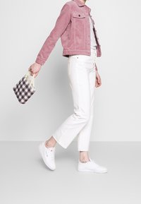 Różowa kurtka z korduroy, szary top, białe spodnie w stylu cropped i białe sneakersy. Nosi małą torebkę w kratkę z koralikowymi uchwytami.