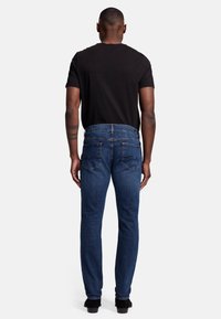 Czarna koszulka i ciemnoniebieskie dżinsy o prostym kroju, z tylnymi kieszeniami i subtelnymi detalami szycia, noszone z czarnymi butami.