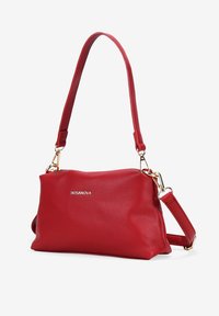 Borsa a tracolla rossa in pelle con superficie testurizzata, hardware dorato, tracolla regolabile e un logo sottile. Forma compatta e rettangolare con bordi arrotondati.