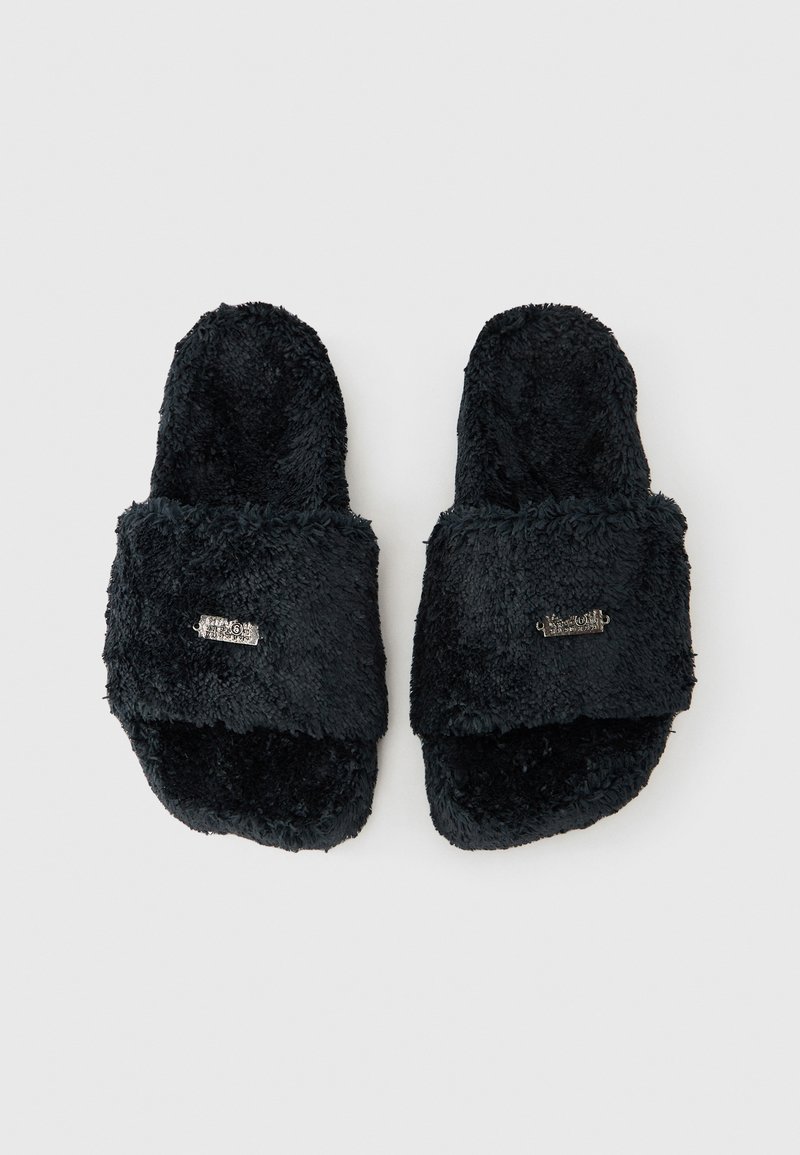 Black fuzzy open-toe slippers with a wide strap and small metallic detail on each strap, laid flat on a white background.