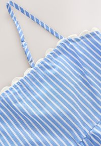 Stropbluse lavet af let stof med lodrette blå og hvide striber. Har bølgede hvide accenter langs kanten. Glat tekstur.