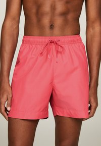 Bañadores en un color rosa brillante, confeccionados en una tela ligera. Cuentan con una pretina elástica con cordón y un dobladillo recto.