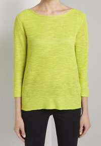 Haut tricoté vert citron à manches trois-quarts avec un motif à rayures horizontales texturées et un large décolleté, associé à un pantalon foncé.