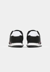 Zwarte sportschoenen met een witte hielcounter, met een soepel bovenwerk, contrasterende rode en roze accenten, en een gestructureerde zwarte rubberen buitenzool.