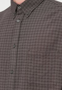 Γκρι πουκάμισο με καρό σχέδιο, κουμπώνει μπροστά, διαθέτει δομημένο γιακά, τσέπη στο στήθος και διακριτική υφή στο ύφασμα.