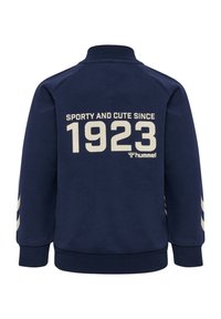 Navy sweatshirt with high collar, ribbed cuffs, and back text reading "SPORTY AND CUTE SINCE 1923" in cream. Three stripes on sleeves.