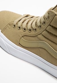 Beige High-Top-Sneaker mit Obermaterial aus Stoff, passenden Schnürsenkeln, seitlichem Streifen-Detail und weißer Gummisohle auf weißem Hintergrund.
