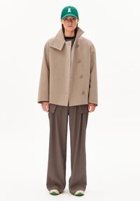 Beige wool blend oversized jacket with large collar, double-breasted buttons, paired with loose brown trousers and green cap with logo.