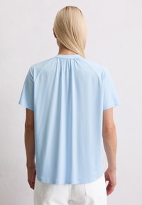 Lichtblauwe T-shirt met korte mouwen en een ronde halslijn, met subtiele plooien aan de achterkant, gemaakt van glad, zacht materiaal.