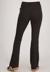 Zwarte flared broek met een gladde textuur, voorzien van twee achterzakken en een middelhoge tailleband. Gestyled met bruine platform sandalen.